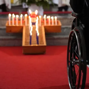 Aufgestelltes Kreuz mit Sand und leuchtenden Kerzen, davor ein Rolli Fahrer