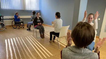 Personen im Raum auf Stühlen und Rollstühlen