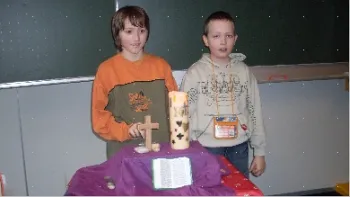 zwei Kinder mit Kreuz und Kerze vor einer Tafel